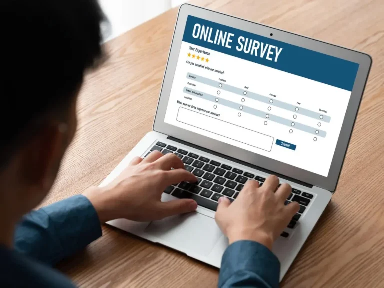 A person sitting at a desk reviewing online survey questions and feedback details on a laptop screen.