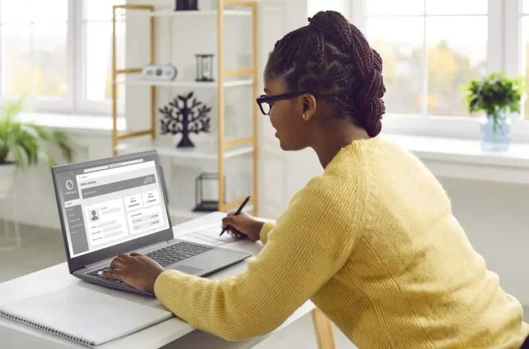 A woman at a desk using a laptop to link her online banking and payout details to complete final account setup instructions.
